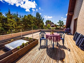 En træterrasse med et bord og stole, omgivet af murstensvægge og udsigt til træer.