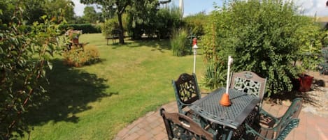 En terrasse med et bord og stole, omgivet af grøn vegetation og et træ.