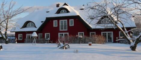 A red house with a snow-covered roof and a snow-covered yard.