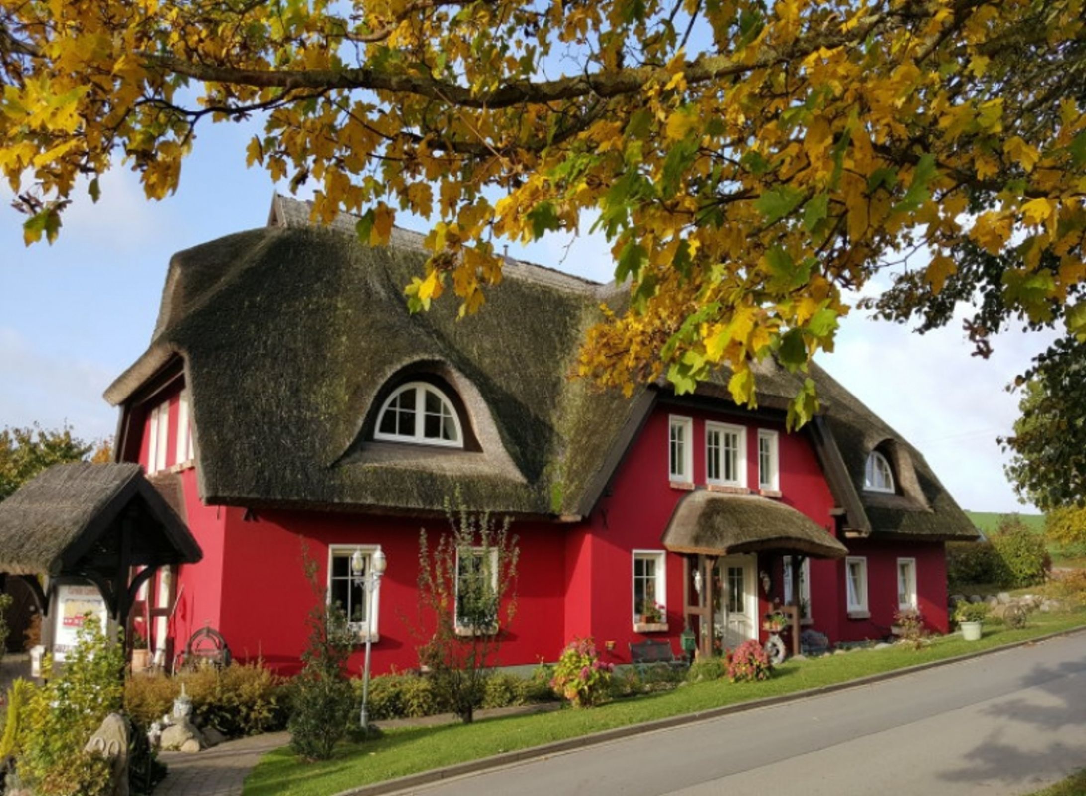 A red house with a thatched roof, surrounded by greenery and a clear sky.