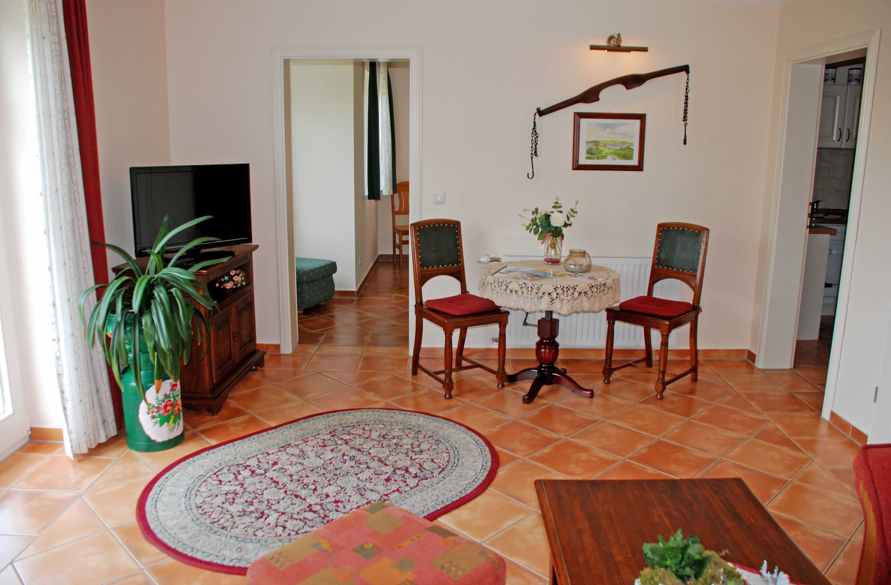 A living room with a television, two chairs, a table, a potted plant, and a rug.