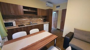 Una cocina compacta con microondas, pileta y un refrigerador pequeño. Hay una mesa de comedor con sillas y un sofá en la zona de estar contigua.