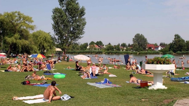 Un parque junto al lago, con gente tomando el sol y nadando.