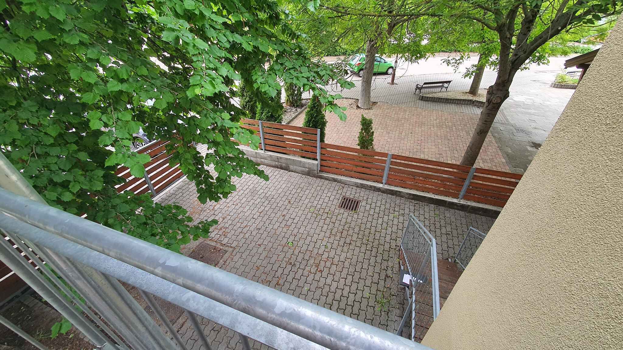 A courtyard with a paved walkway, a wooden bench, and a metal railing.