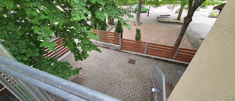 A courtyard with a paved walkway, a wooden bench, and a metal railing.