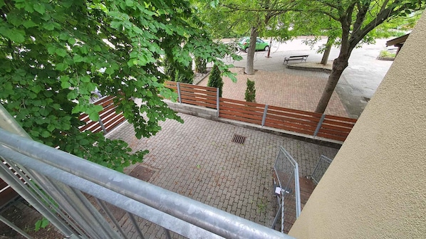 A courtyard with a paved walkway, a wooden bench, and a metal railing.
