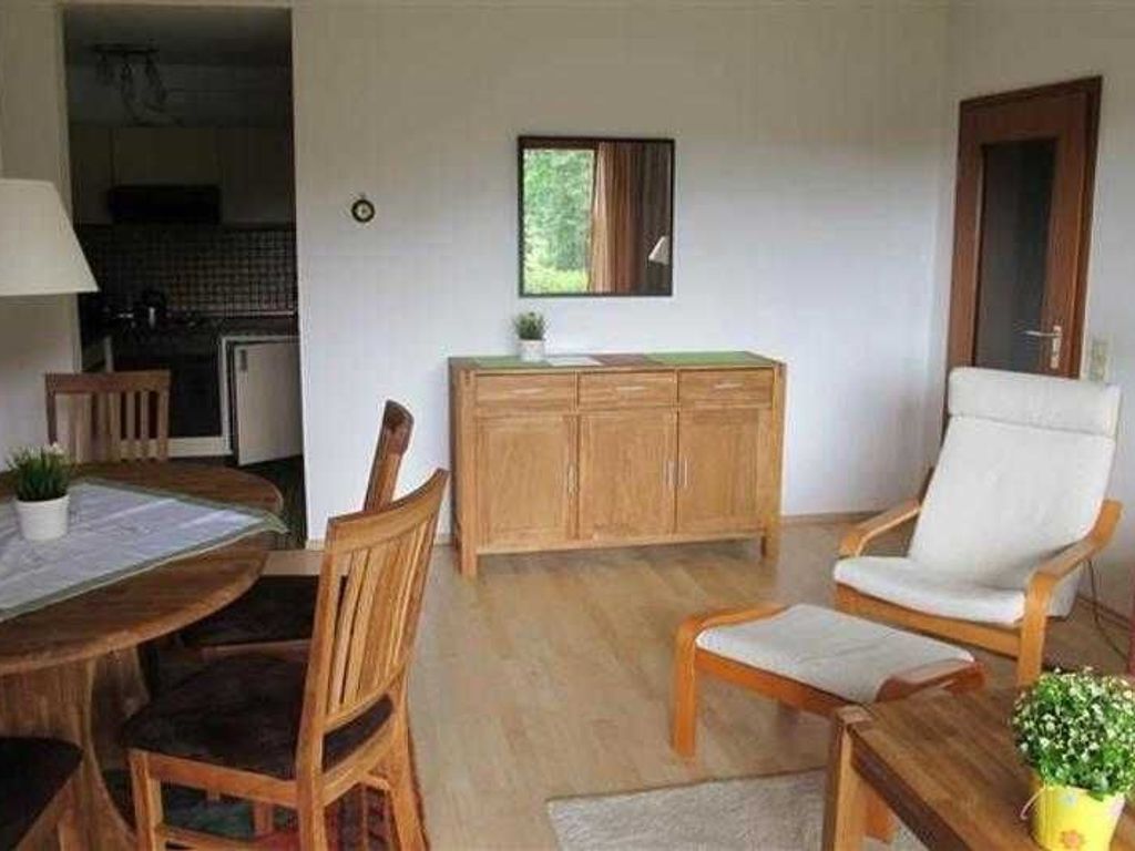 Une pièce comprenant une table à manger en bois, deux chaises, un buffet en bois, un fauteuil blanc et une petite plante en pot.