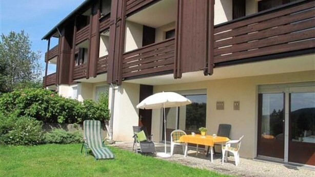 A two-story building with a balcony, a patio with outdoor furniture, and a well-maintained lawn.