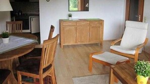A room with a wooden dining table, two chairs, a wooden cabinet, a white armchair, and a small potted plant.