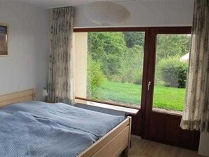 A bedroom with a bed, a window, and a door leading to a garden.