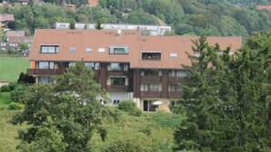 A multi-story residential building with a flat roof, multiple balconies, and a garden area in front.