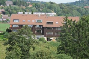 A multi-story residential building with a flat roof, multiple balconies, and a garden area in front.