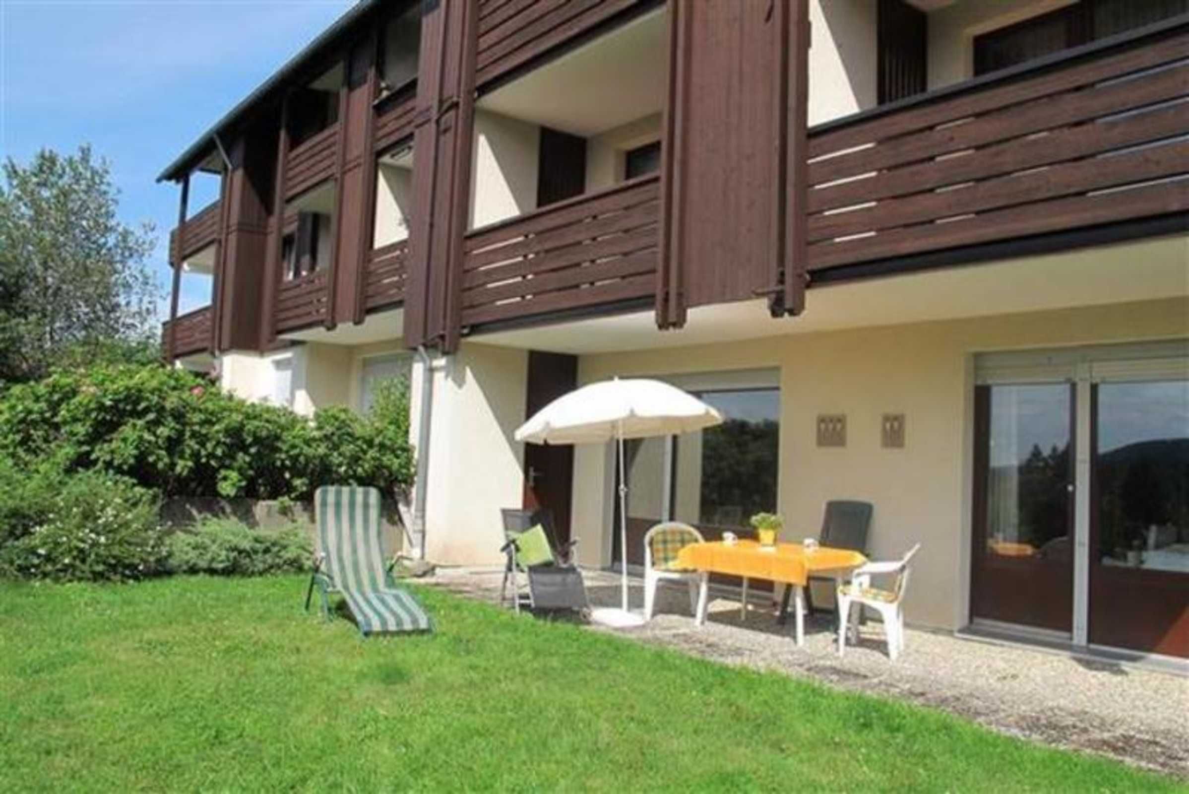 A two-story building with a balcony, a patio with outdoor furniture, and a well-maintained lawn.