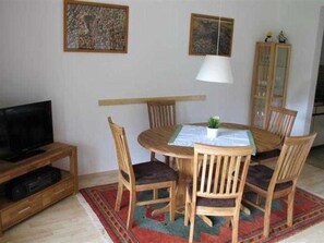 A dining area with a round table, four chairs, a television on a stand, and two framed pictures on the wall.