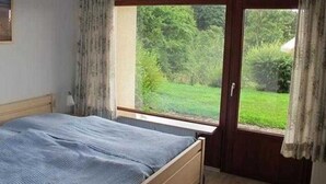 A bedroom with a bed, a window, and a door leading to a garden.