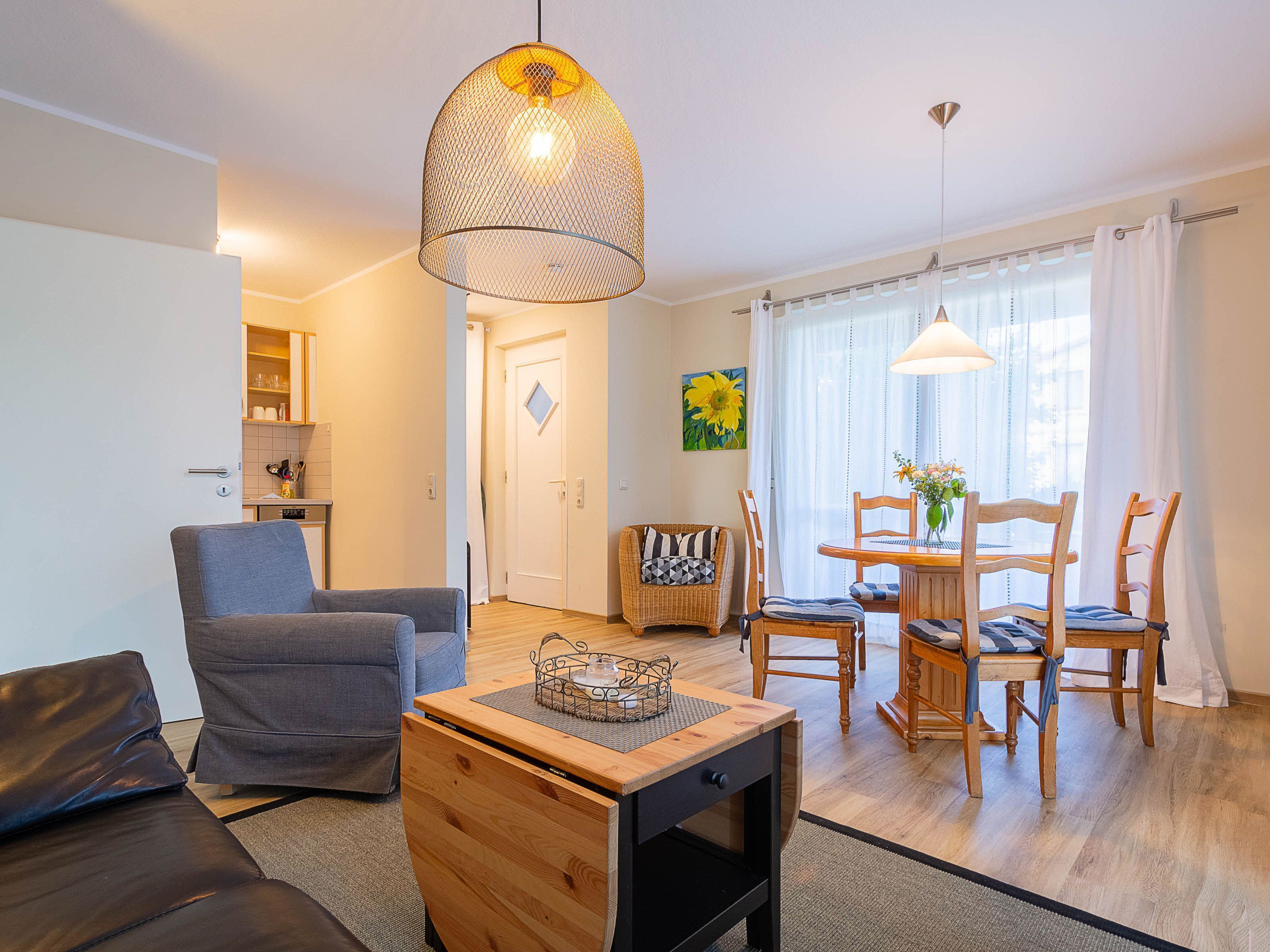Ett modernt vardagsrum med en soffa, ett soffbord i trä, ett matbord med stolar och ett köksområde i bakgrunden.