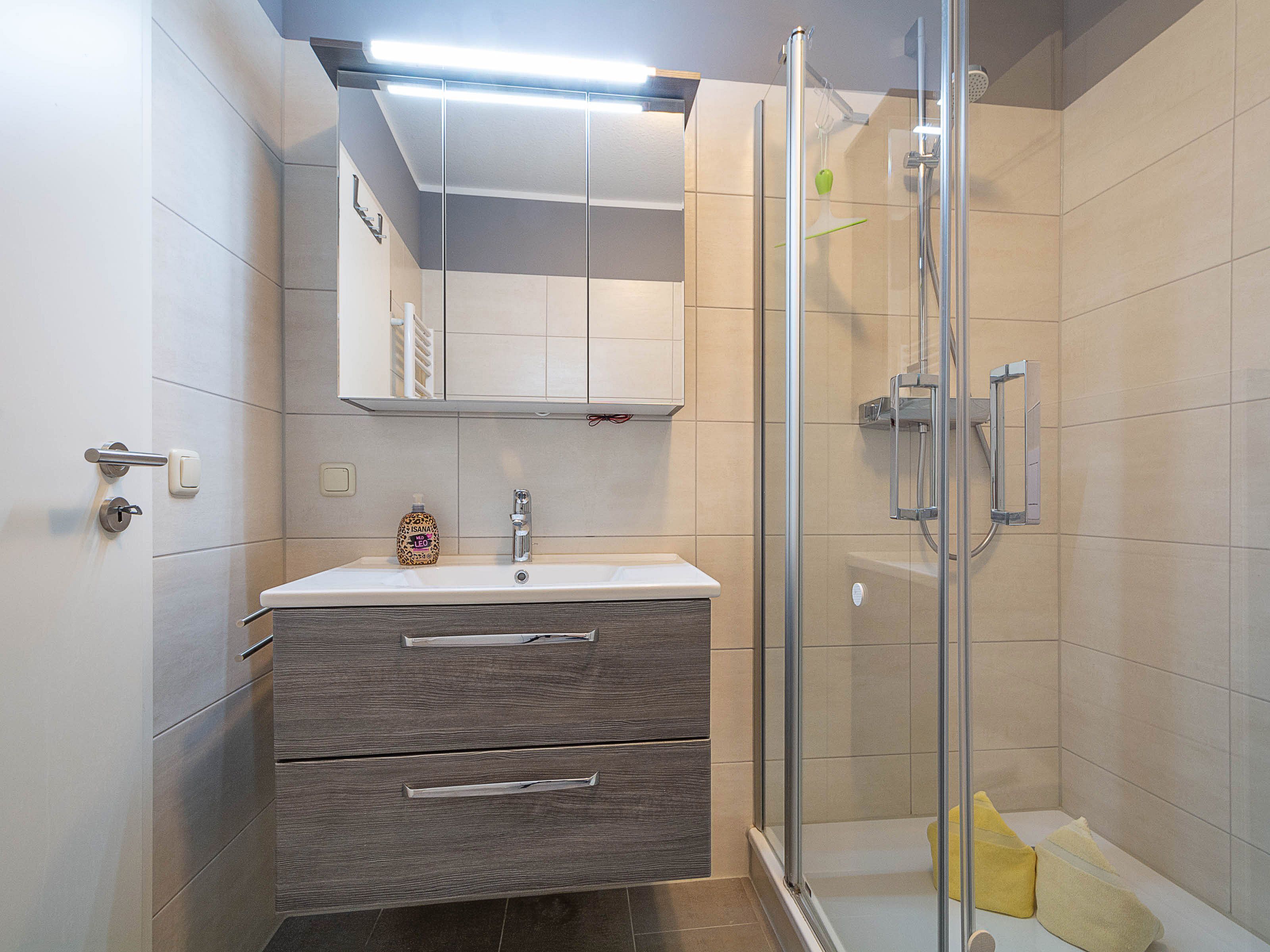 Un baño moderno con ducha de vidrio, tocador con espejo y inodoro.