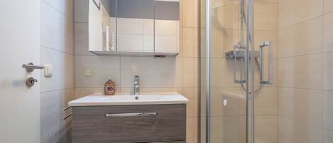Un baño moderno con ducha de vidrio, tocador con espejo y inodoro.