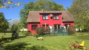 A red house with a tiled roof, surrounded by a well-maintained lawn and trees.