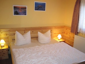 Una cama con ropa de cama blanca, dos almohadas, un cabecero de madera, dos lámparas de noche y dos cuadros en la pared.