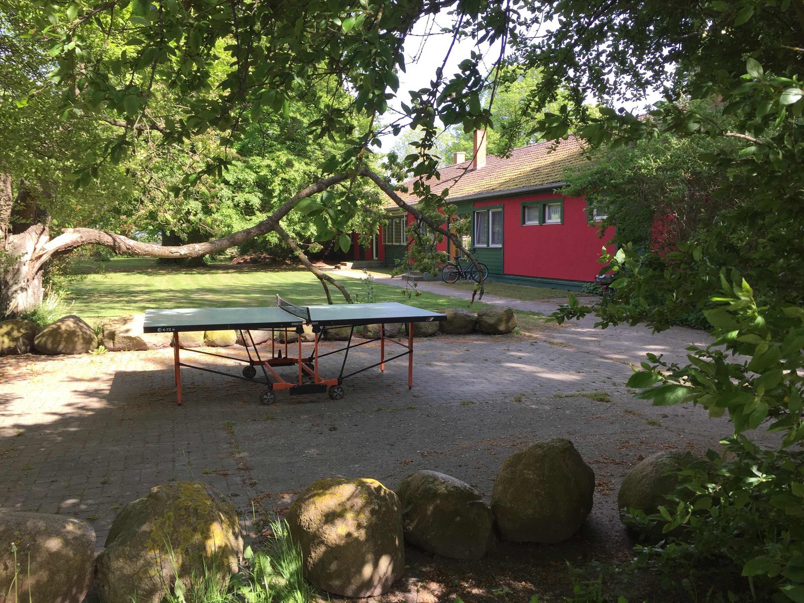 Une table de ping-pong dans un jardin, avec un bâtiment rouge en arrière-plan.