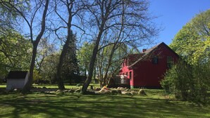 A red house with a sloped roof, surrounded by a grassy yard with trees and a small shed.