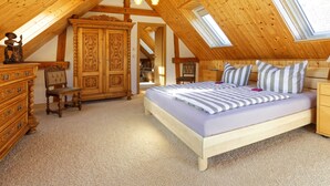 A bedroom with a sloped ceiling, wooden furniture, a bed with striped bedding, and a large wardrobe. - Small cottage on the forest and hunting lodge - Forest & Jagdgut (Lütow)