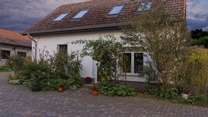 A house with a tiled roof, two skylights, and a garden with various plants and flowers. - Small cottage on the forest and hunting lodge - Forest & Jagdgut (Lütow)