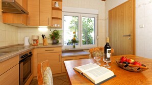 A kitchen with wooden cabinets, a dining table with a book, wine glass, and fruit bowl. - Small cottage on the forest and hunting lodge - Forest & Jagdgut (Lütow)