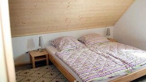 Une petite chambre avec un lit simple, un plafond en pente, une table de chevet et une couvre-lit à motifs.