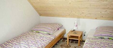Ein kleines, einfaches Zimmer mit zwei Holzbettställen, einem kleinen Nachttisch und einem Teppich.