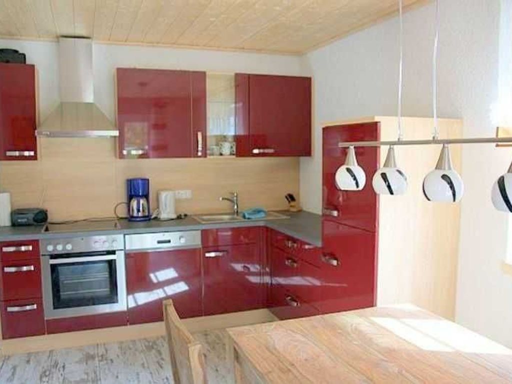 Una cocina con armarios rojos, una estufa y ollas colgando.
