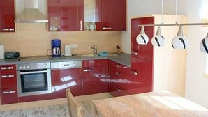 Une cuisine avec des placards rouges, un fourneau et des casseroles suspendues.