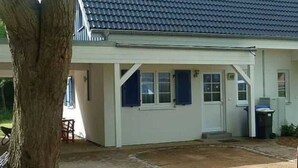Un bâtiment d’un seul étage, doté d’un toit recouvert de tuiles sombres, de murs extérieurs blancs et d’une porte d’entrée avec un petit porche.