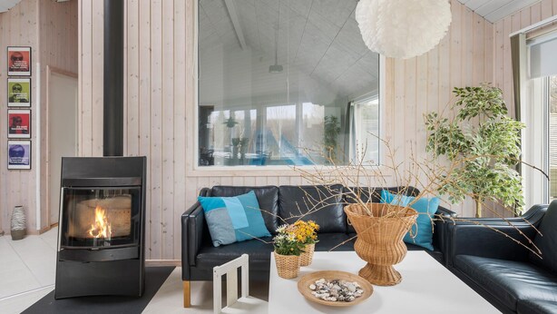 A modern living room with a fireplace, a black leather sofa, a white coffee table, and a large window with a view. - Gorgeous home in Tisvildeleje with sauna (Tisvildeleje)