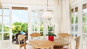 Een eetruimte met een ronde houten tafel, zes stoelen en een rode vaas met witte bloemen.