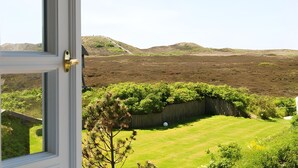 Uitzicht vanuit een raam op een gazon met een houten omheining, een boom en heuvels in de verte.