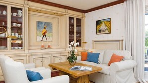 Een woonkamer met een witte bank, een houten salontafel en een kast met glaswerk.