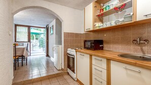 A compact kitchen with a microwave, stove, and sink. There is a dining area with a table and chairs visible through an archway.