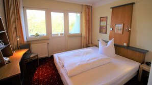 Ein Hotelzimmer mit einem großen Bett, einem Schreibtisch mit Stuhl, einem Heizkörper und einem Fenster mit Vorhängen.