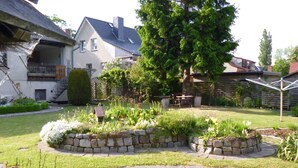 Un jardín residencial con bordes de piedra, un árbol grande y una casa con balcón.