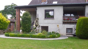 Una casa de dos pisos con un balcón, una chimenea y un jardín bien cuidado.