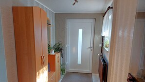 Un pasillo con un armario de madera, una puerta, un pequeño mueble con una planta y un radiador.