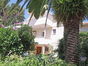 Un edificio a due piani con un balcone, immerso nel verde rigoglioso e con una palma.