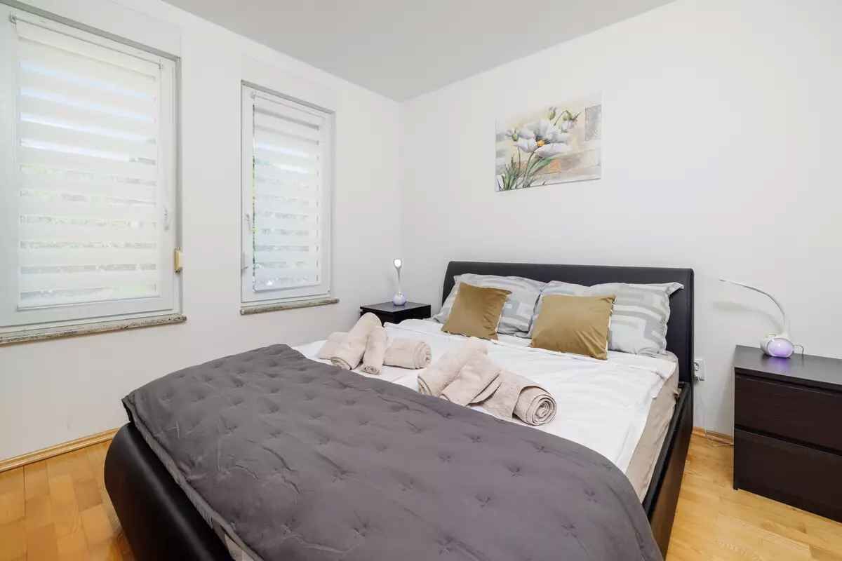 Een slaapkamer met een bed, kussens, een nachtkastje en een wandlamp.