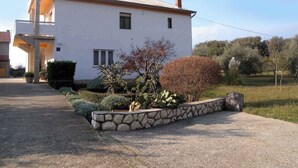 A two-story house with a stone pathway leading to the entrance, surrounded by various plants and cacti. - Holiday apartment with terrace (Kampor)