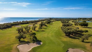 Vista aérea de un campo de golf con búnkeres de arena, árboles y una masa de agua al fondo.