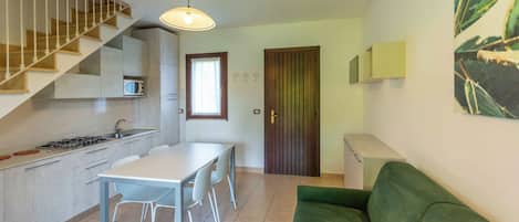 Una cucina funzionale con un tavolo da pranzo, sedie, un divano verde, una scala e una porta con una finestra.