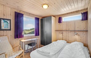 Et rum med træpaneler, seng, skrivebord, stol og garderobeskab.
