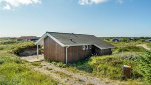 A wooden cabin with a sloped roof, surrounded by natural vegetation and a clear sky.